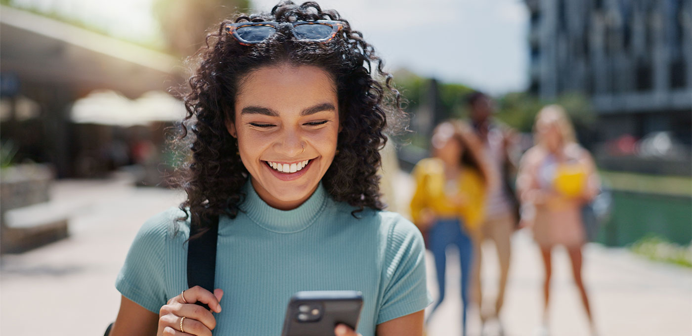 College student smiles looking at phone while viewing First State Bank digital banking app